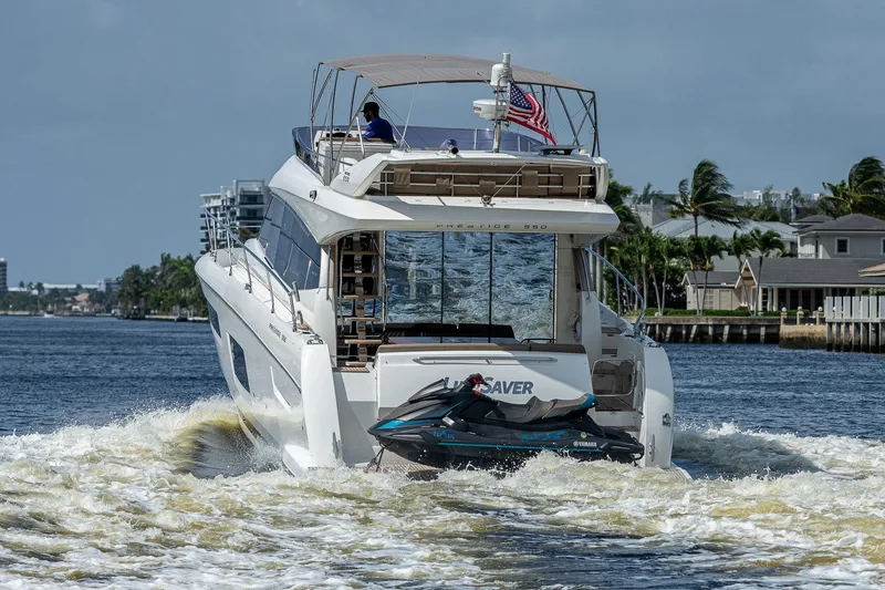 Slide: The Image of Luxury 2014 Prestige 550 yacht cruising with jet ski, American flag, and scenic waterfront view. - 18