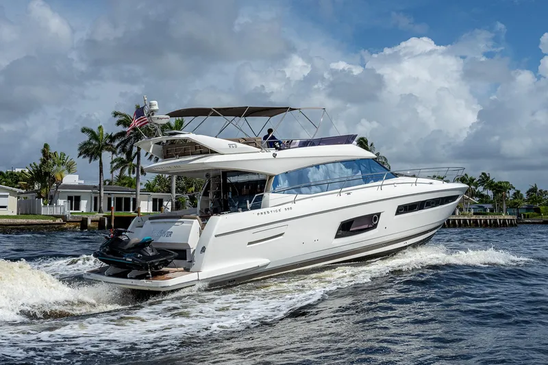 Slide: The Image of 2014 Prestige 550 yacht cruising on a sunny day, with palm trees in the background. - 31