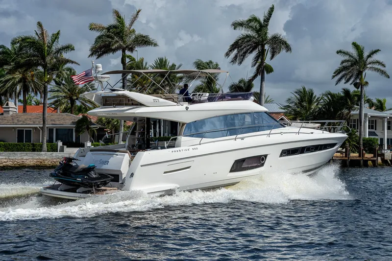 Slide: The Image of 2014 Prestige 550 yacht cruising on a sunny day with palm trees in the background. - 42