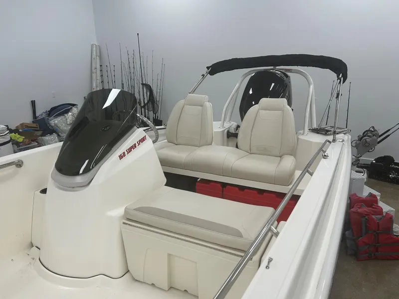 Slide: The Image of 2020 Boston Whaler 160 Super Sport boat with white seating and black canopy in a garage. - 3