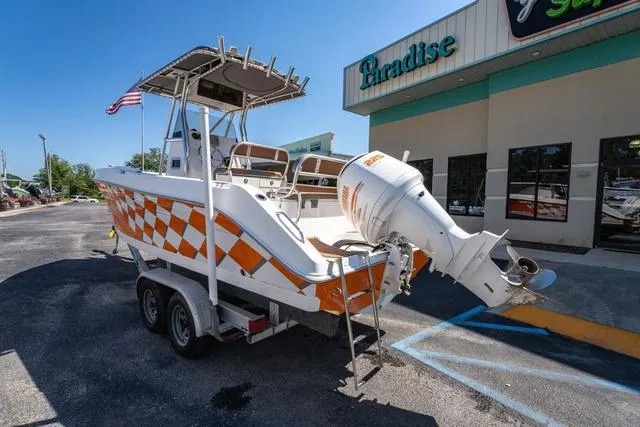 Slide: The Image of 2004 Cobia 234 boat with orange checkered design on trailer outside Paradise store. - 3