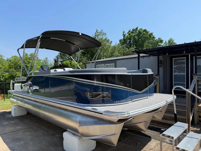 Slide: The Image of 2025 Avalon LSZ Cruise Bench pontoon boat with canopy, parked outdoors on a sunny day. - 1