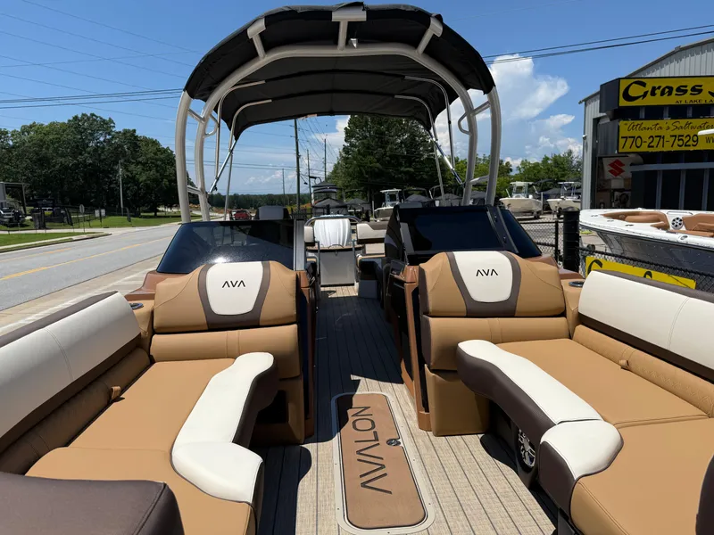 Slide: The Image of 2025 Avalon Catalina Quad Lounger Windshield boat with luxurious seating and canopy, parked outdoors. - 13