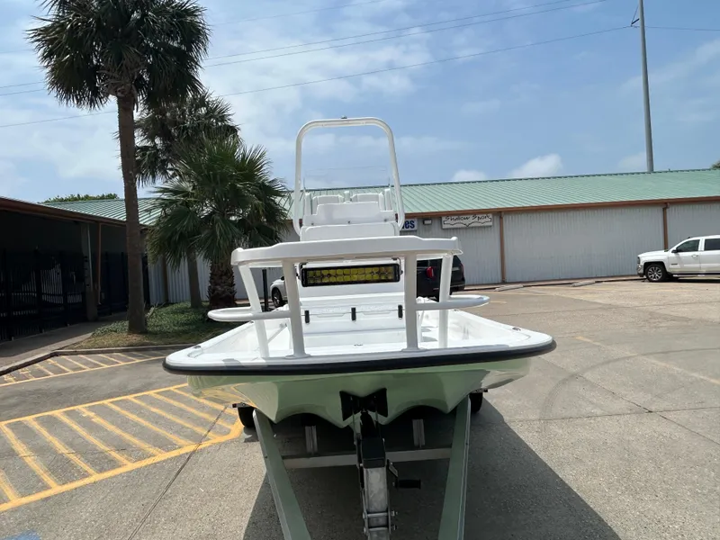 Slide: The Image of 2023 Shallow Sport 21 Sport boat on trailer in parking lot, palm tree nearby. - 2