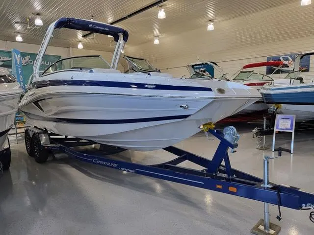 Slide: The Image of 2024 Crownline E260 XS boat on trailer in showroom, featuring sleek design and blue accents. - 2