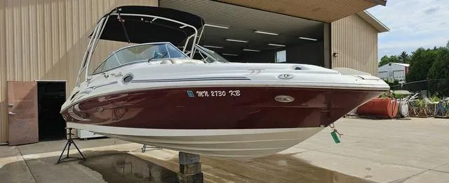 Slide: The Image of 2006 Sea Ray 270 Sundeck boat with maroon hull, docked near a warehouse. - 12