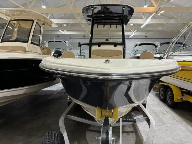 Slide: The Image of 2025 Scout 215 XSF boat on trailer in showroom, surrounded by other boats. - 2