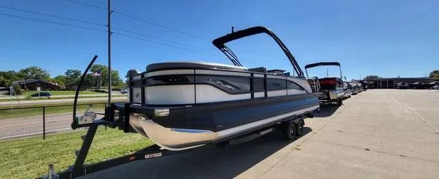 Slide: The Image of 2024 Barletta Corsa 25UEA pontoon boat on trailer, parked outdoors under clear blue sky. - 1