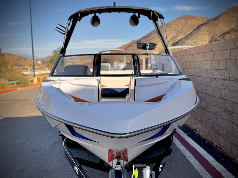 Slide: The Image of 2021 Axis T22 boat on trailer, parked near mountains and brick wall. - 2