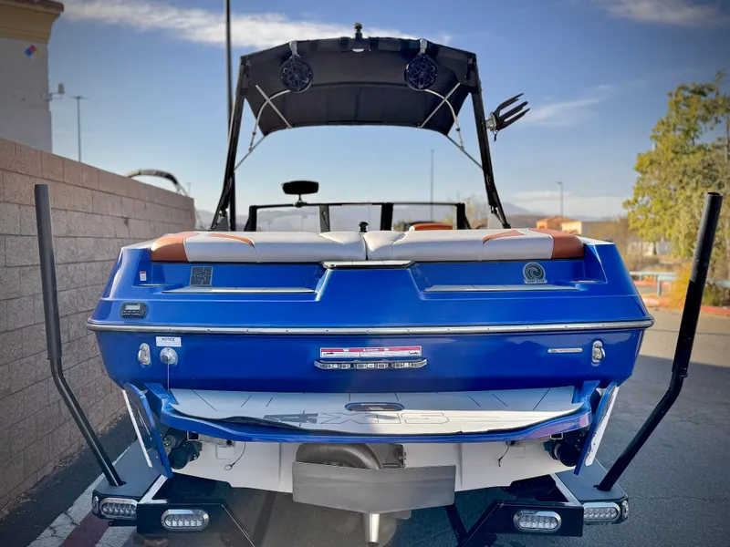 Slide: The Image of 2021 Axis T22 boat, blue exterior, rear view with speakers and seating, parked outdoors. - 4