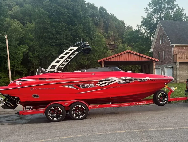 The Image of Red 2022 Crownline 240 SS LPX boat on trailer, parked near house and trees. - 1
