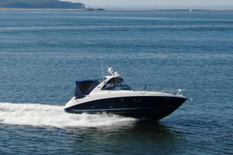 The Image of 2012 Sea Ray 310 Sundancer cruising on open water, scenic coastal backdrop. - 0