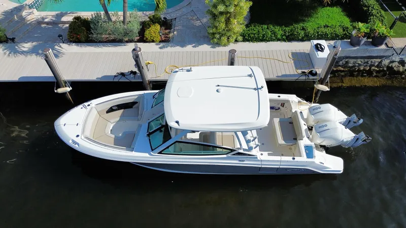 Slide: The Image of 2023 Boston Whaler 280 Vantage boat docked by a waterfront with lush greenery. - 3