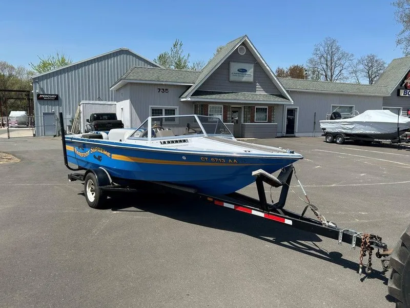 Slide: The Image of 1980 Ski Supreme boat on trailer in parking lot, near gray building. - 2