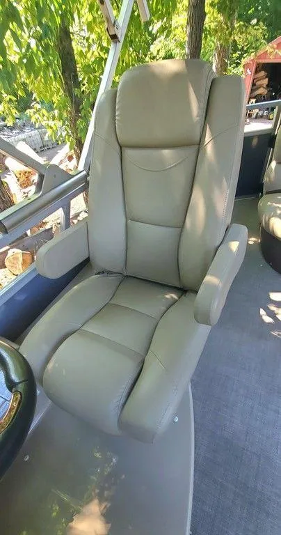 Slide: The Image of Comfortable captain's chair on 2017 Regency 220 DL3 boat, surrounded by lush greenery. - 23