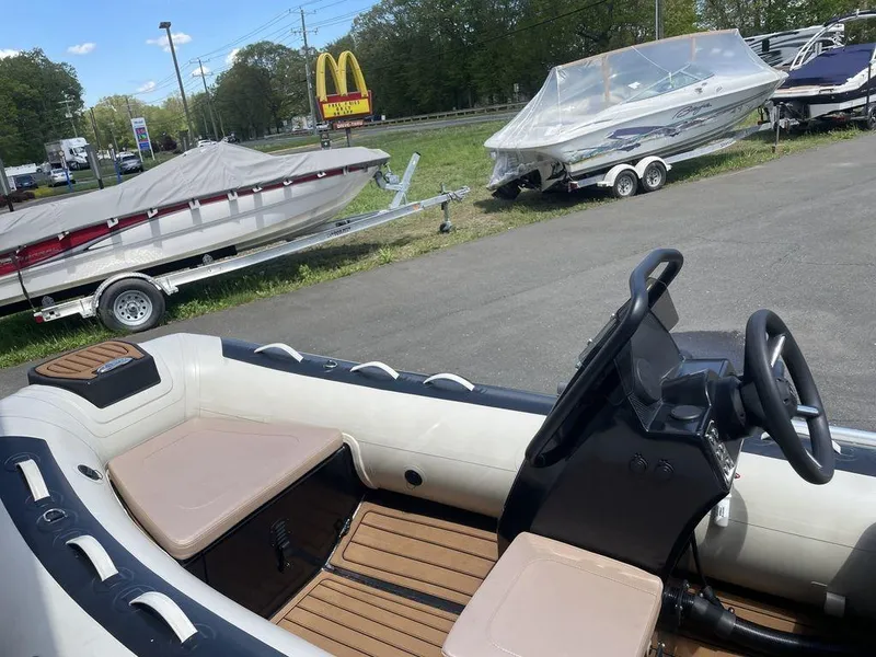 Slide: The Image of 2023 Highfield Classic 380 GT Limited boat interior with steering wheel and seating, parked near trailers. - 2