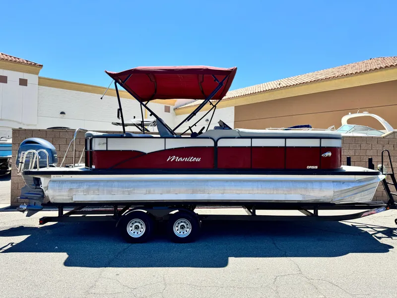 Slide: The Image of 2019 Manitou 23 Oasis pontoon boat with red canopy on a trailer. - 0
