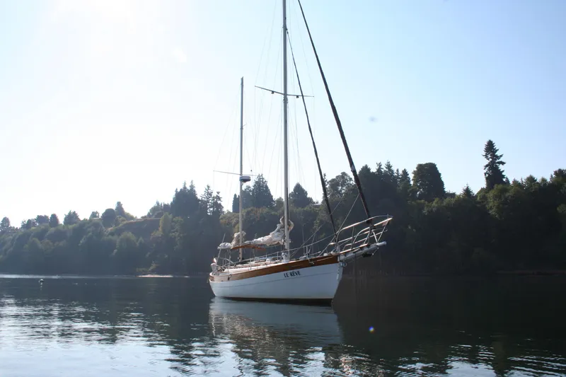 The Image of 1979 Hans Christian 38 Ketch sailboat on calm water, surrounded by trees. - 1
