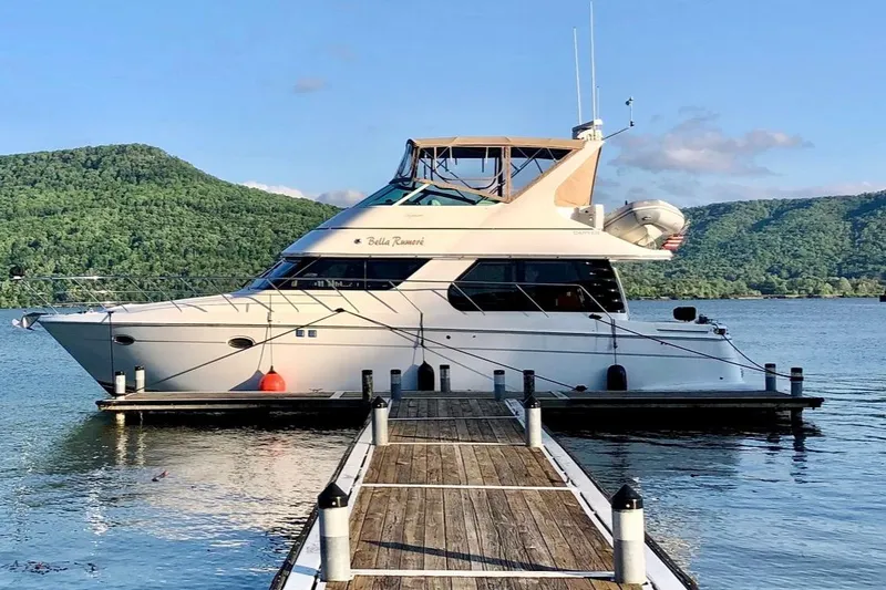 The Image of 2000 Carver 450 Voyager Pilothouse yacht docked on a serene lake with lush hills. - 1