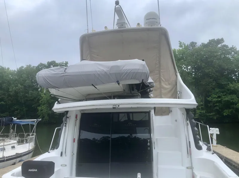 Slide: The Image of 2000 Carver 450 Voyager Pilothouse yacht docked, featuring upper deck and covered dinghy. - 8