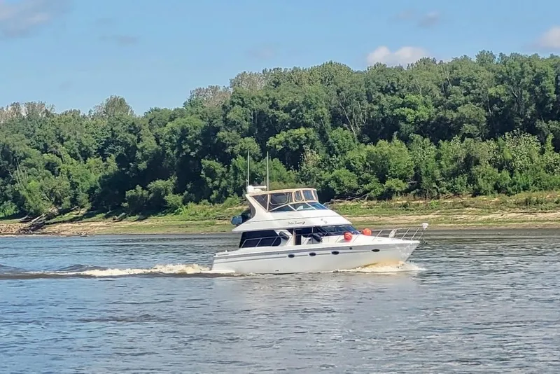 Slide: The Image of 2000 Carver 450 Voyager Pilothouse cruising on a river with lush green forest backdrop. - 2