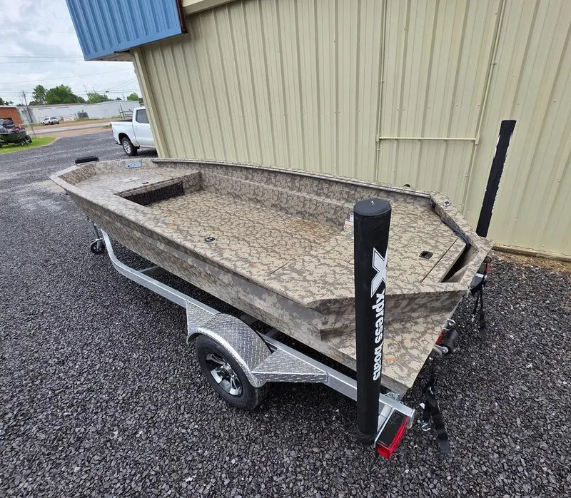 Slide: The Image of 2025 Xpress H18DB boat on trailer, camo design, parked on gravel near building. - 12