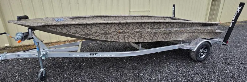 Slide: The Image of 2025 Xpress H18DB boat on trailer, camouflage design, parked on gravel. - 18