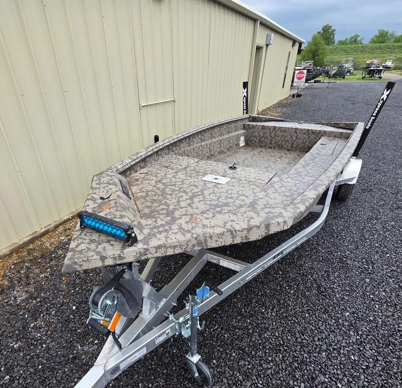 Slide: The Image of 2025 Xpress H18DB boat on trailer, camo design, parked outside a building. - 21