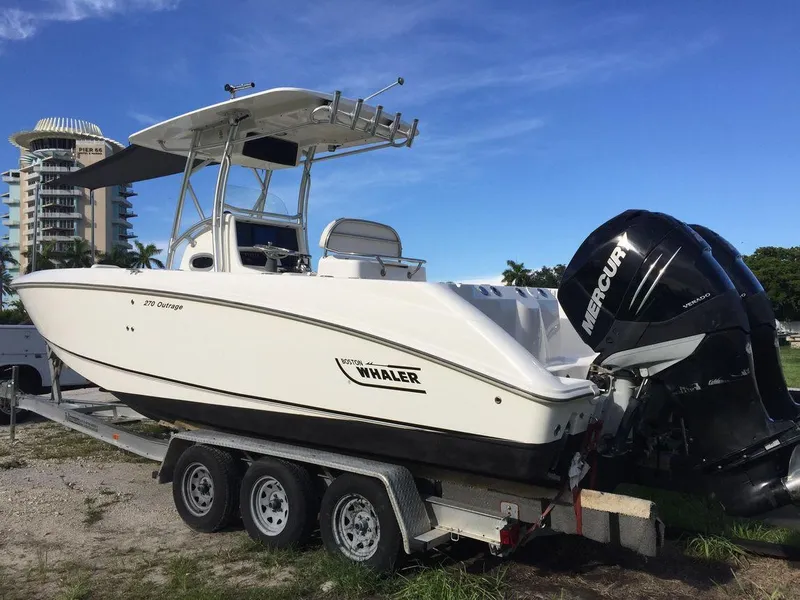 The Image of 2006 Boston Whaler 270 Outrage boat on trailer with Mercury outboard, parked outdoors. - 1