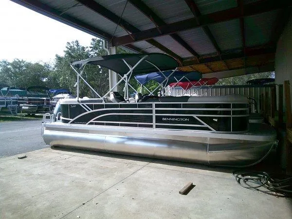 Slide: The Image of 2025 Bennington 22SSR pontoon boat under a metal canopy, parked on concrete. - 1
