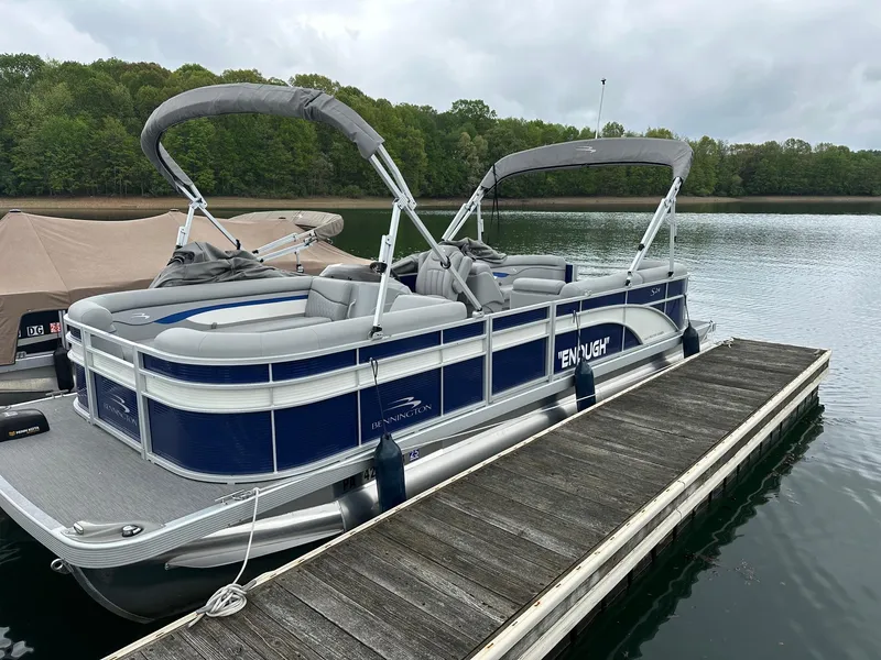 Slide: The Image of 2022 Bennington 24 SSR Quad Bench pontoon boat docked on a calm lake. - 1