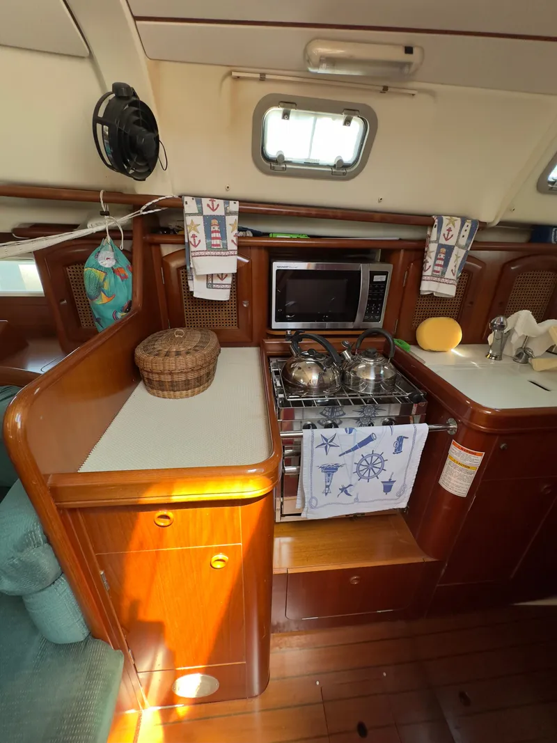 Slide: The Image of Interior of 2000 Beneteau 411 sailboat kitchen with stove, microwave, and wooden cabinetry. - 27