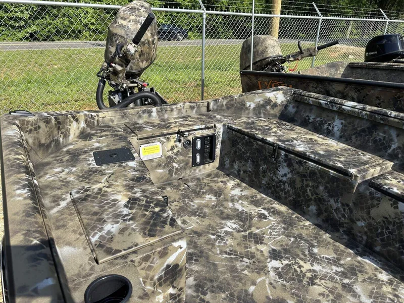 Slide: The Image of Camouflage-patterned 2025 Excel Viper F4 1751 boat interior with motor, parked near a chain-link fence. - 10