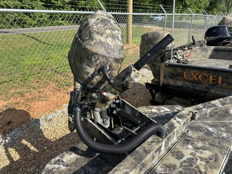 Slide: The Image of 2025 Excel Viper F4 1751 boat with camo design and outboard motor, parked near a fence. - 6