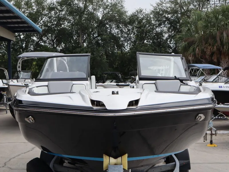 Slide: The Image of 2021 Yamaha Boats 212, sleek design, parked outdoors, surrounded by trees and other boats. - 3