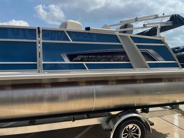 Slide: The Image of 2025 Starcraft EX20QDH pontoon boat with blue paneling and sleek design on a trailer. - 5