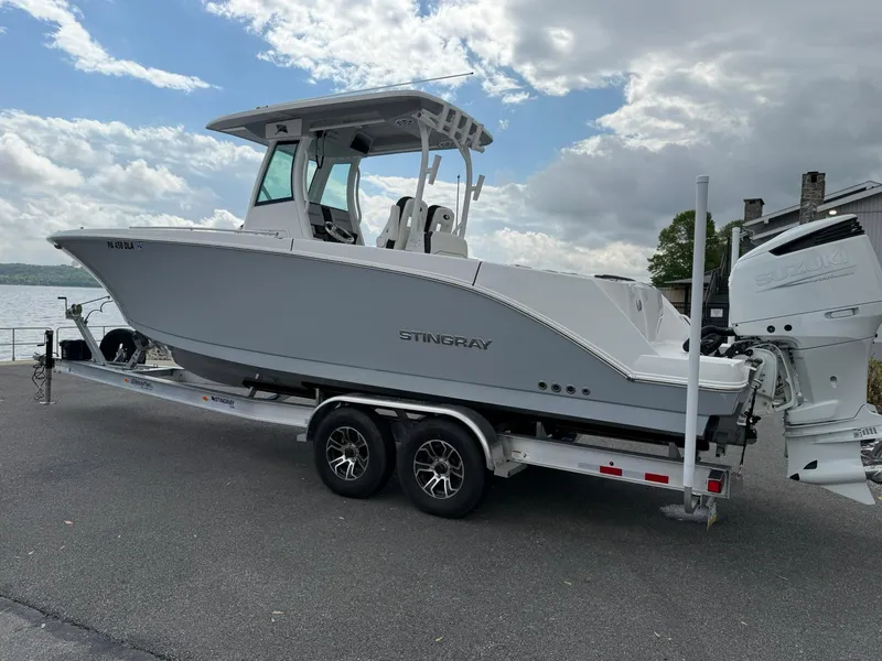 Slide: The Image of 2025 Stingray 273 CC boat on trailer, parked by waterfront under cloudy sky. - 2
