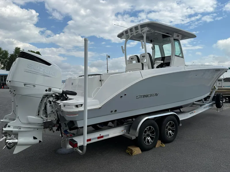 Slide: The Image of 2025 Stingray 273 CC boat on trailer, white exterior, dual engines, parked outdoors. - 5