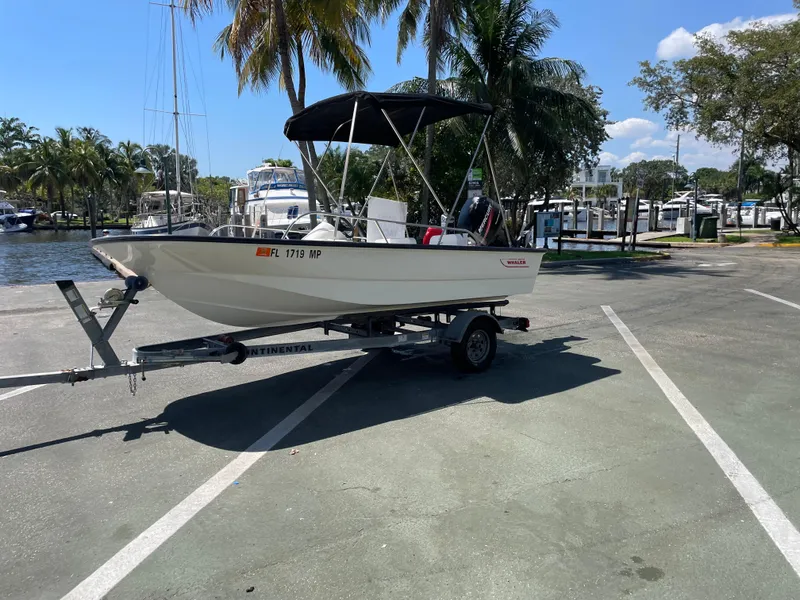 Slide: The Image of 2004 Boston Whaler 150 Sport boat on trailer, parked near marina with palm trees. - 11