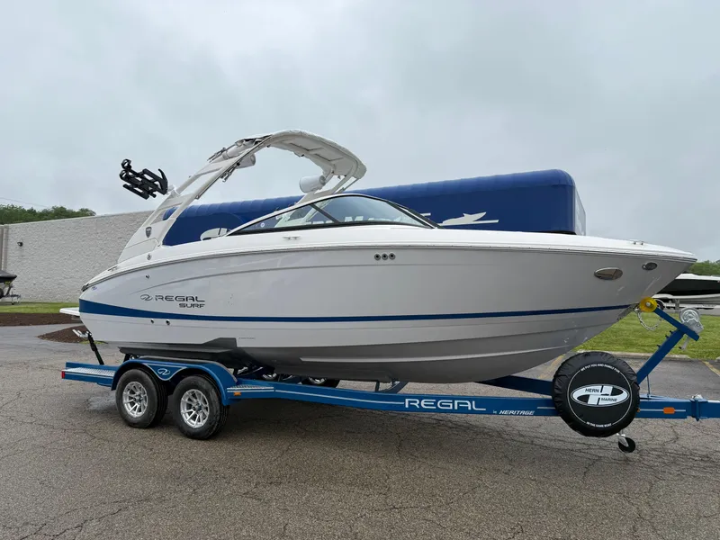 The Image of 2025 Regal LS4 Surf boat on trailer, white and blue design, parked outdoors. - 0