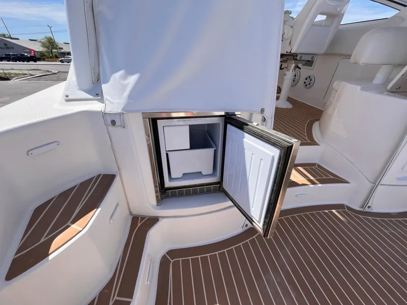 Slide: The Image of 2021 Fountain 38 SFC boat interior with open mini fridge, white seating, and wood-patterned flooring. - 26