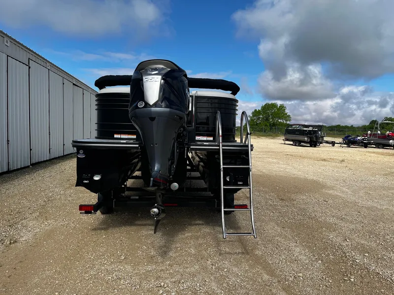 Slide: The Image of 2025 SunCatcher Elite 324 RC boat with outboard motor, parked on gravel near storage units. - 6