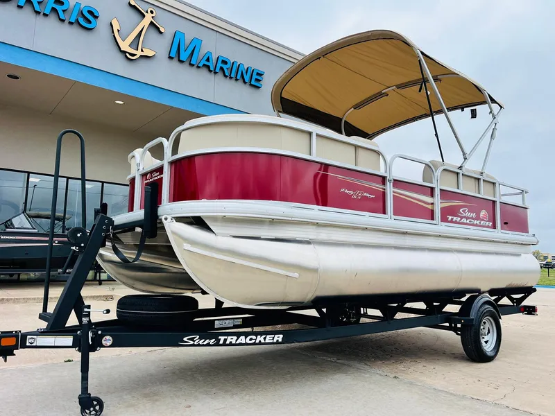 Slide: The Image of 2025 Sun Tracker Party Barge 18 DLX pontoon boat on trailer outside marine dealership. - 3