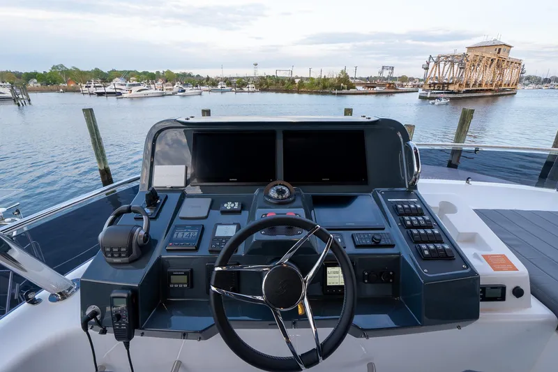 Slide: The Image of 2024 Sirena 58 Flybridge helm with dual screens, steering wheel, and waterfront view. - 31