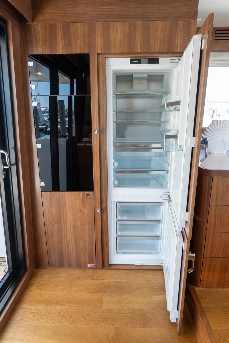 Slide: The Image of 2024 Sirena 58 Flybridge yacht interior with open refrigerator, wooden flooring, and modern design. - 42