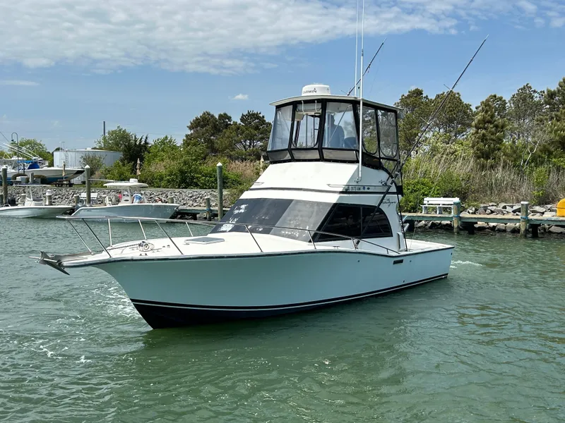 Slide: The Image of 1990 Albemarle 325 Convertible boat on water, docked near lush greenery and clear sky. - 4