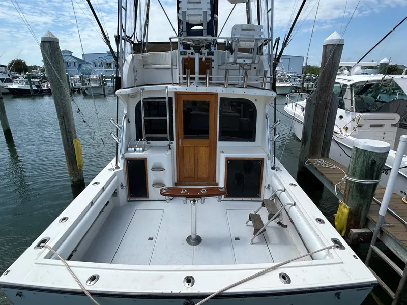 Slide: The Image of 1990 Albemarle 325 Convertible boat docked at marina, featuring spacious deck and wooden door. - 7