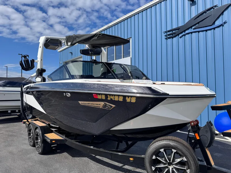 Slide: The Image of 2022 Nautique Super Air Nautique G21 boat on trailer, parked by blue building. - 2