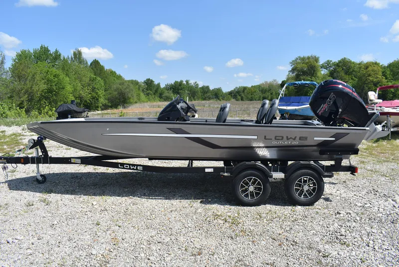 Slide: The Image of 2025 Lowe Outlet 20 boat on trailer, parked outdoors on gravel, with trees in background. - 4
