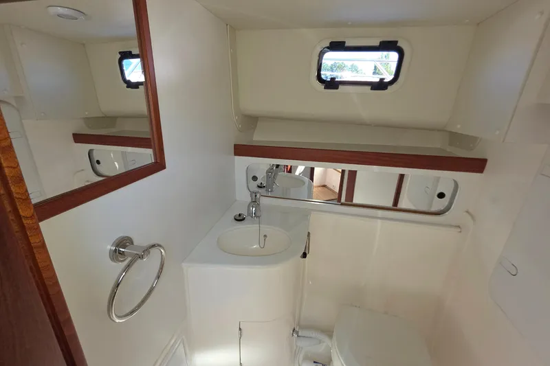 Slide: The Image of 2024 NorthCoast 315 HT boat bathroom with sink, mirror, and porthole window. - 27